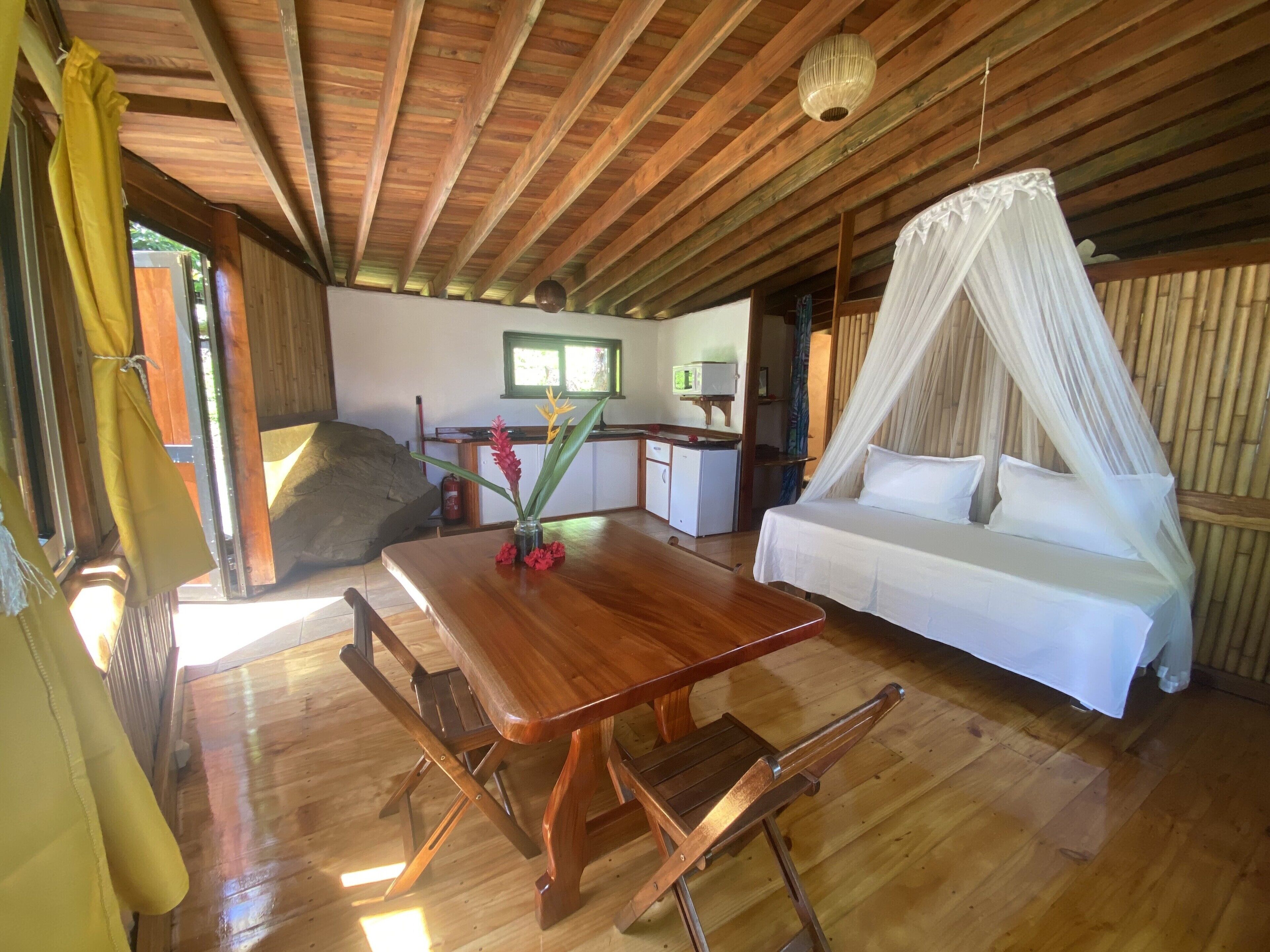 Una habitación con suelo de madera, una cama, una mesa de comedor y una zona de cocina.