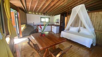 Una habitación con suelo de madera, una cama, una mesa de comedor y una zona de cocina.