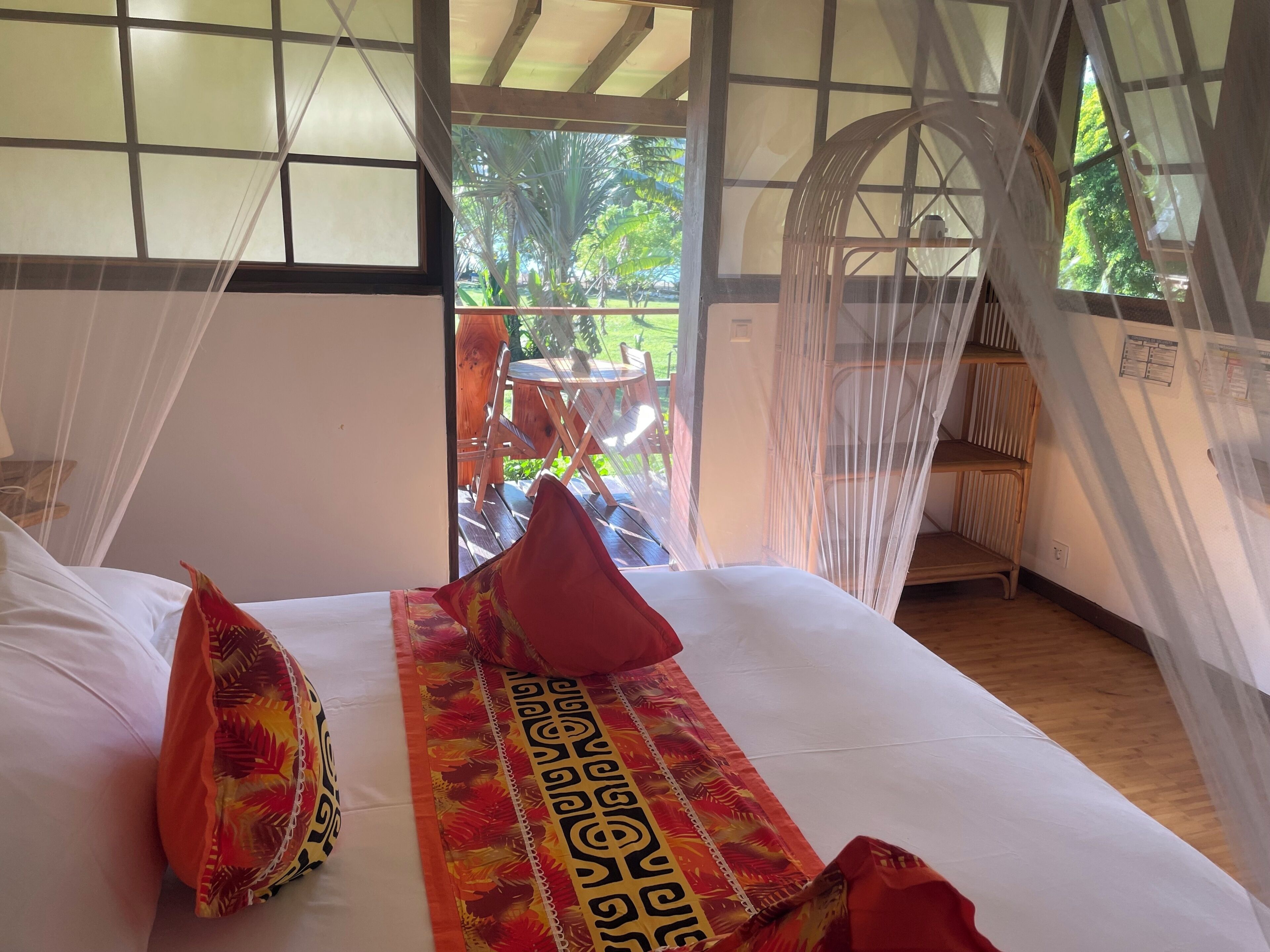 A bed with white linens, red pillows, and a decorative pillow with a tropical pattern.