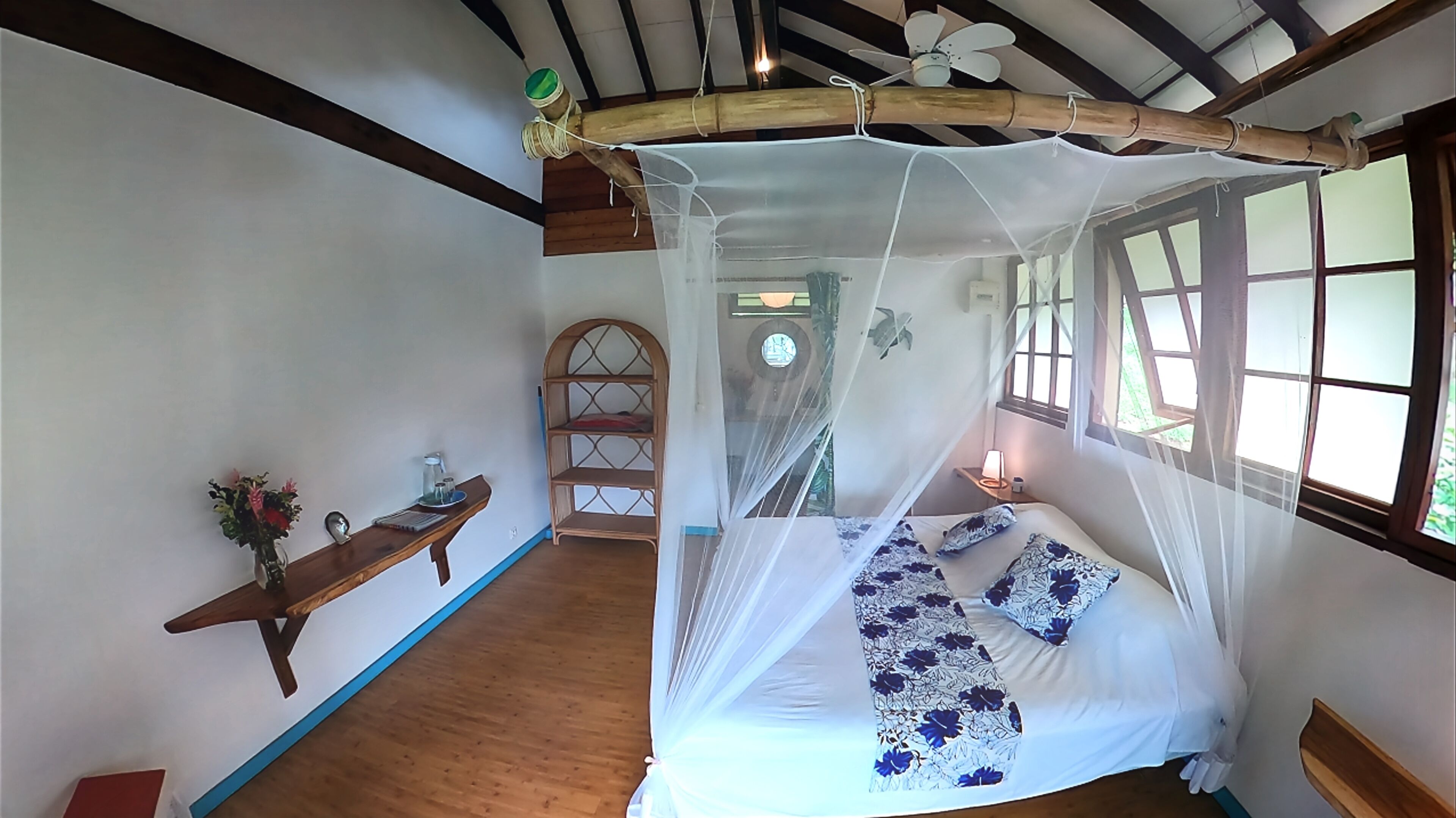 Ein Schlafzimmer mit Baldachinbett, einer Holzwand mit Dekoration, einer Holzlade und einem Fenster mit Blick auf Grünflächen.
