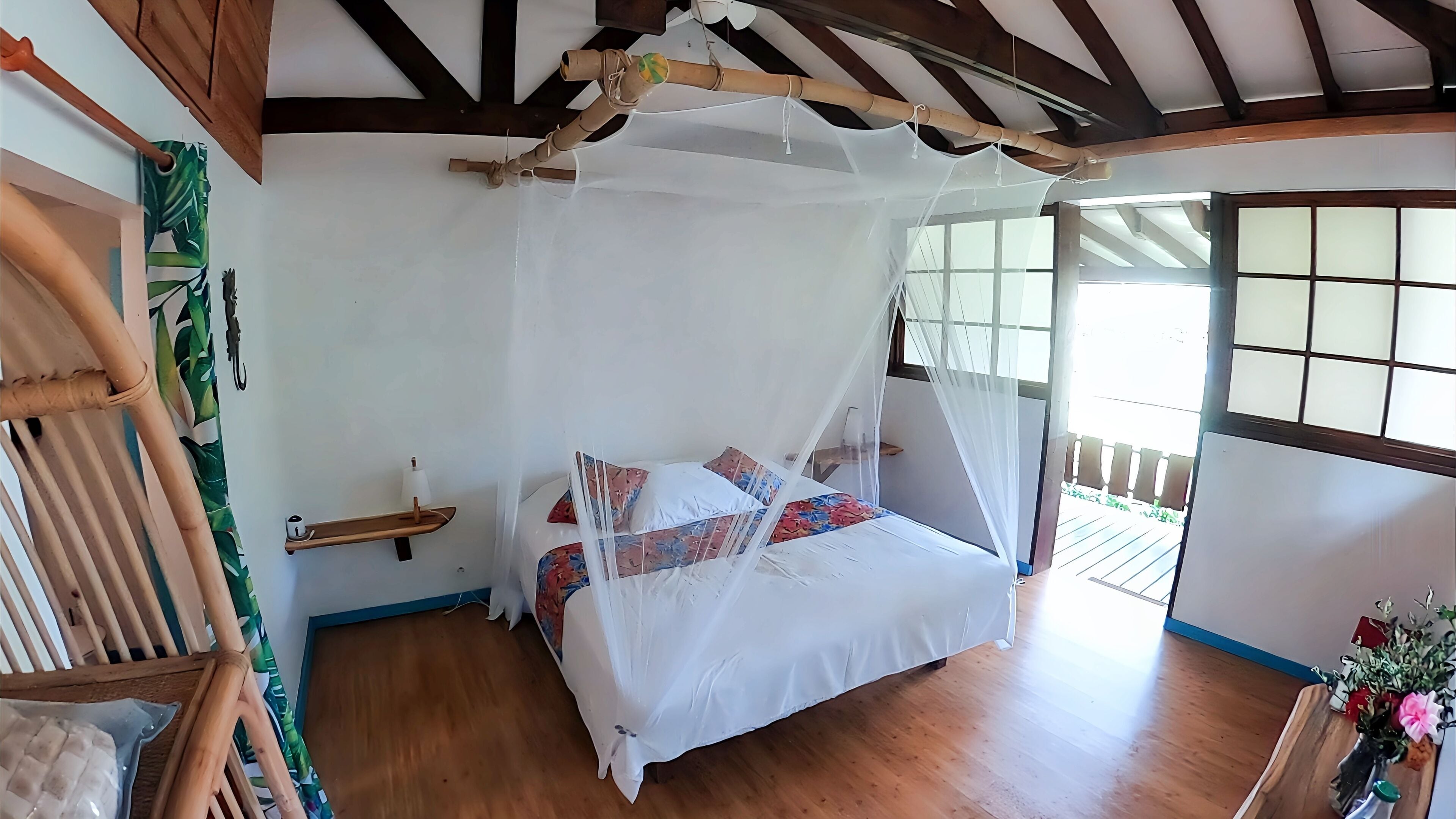 Una habitación con cama bajo dosel, vigas de madera en el techo, piso de madera y ventana con vista.