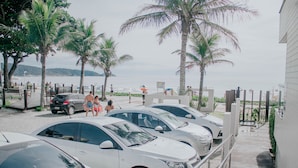 A parking area with several white cars, palm trees, and a view of the beach. - Pousada Garatéia (Bombinhas)