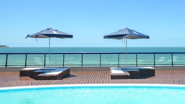A poolside area with two lounge chairs and umbrellas, overlooking the sea. - Pousada Garatéia (Bombinhas)