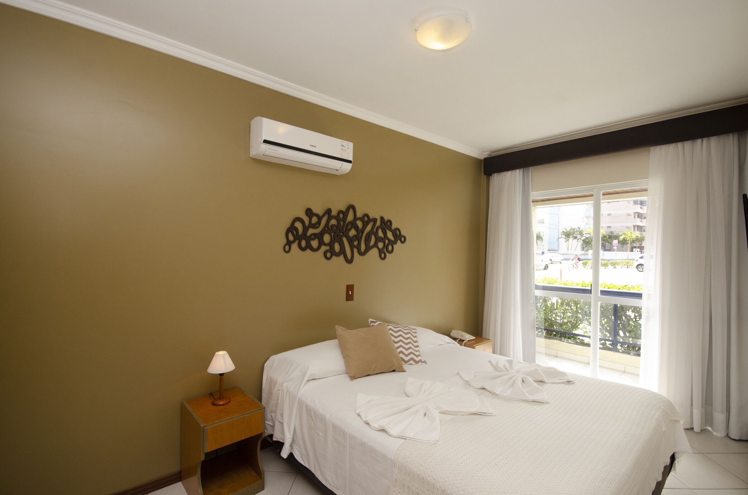 Habitación de hotel con cama, mesita de noche, aire acondicionado, un adorno en la pared y vistas al exterior.
