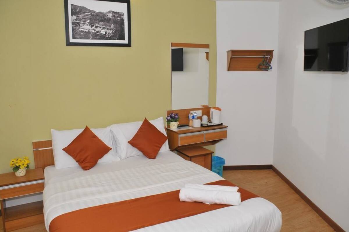 Une chambre d’hôtel bien rangée, avec un lit, une table de chevet et un petit bureau doté d’un miroir.