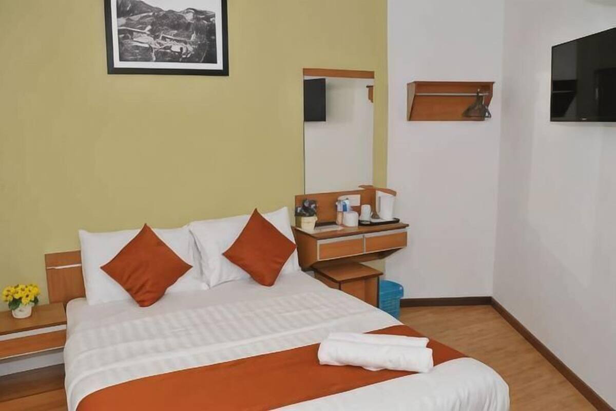 Habitación de hotel con cama, mesita de noche, espejo, televisión y un cuadro en la pared.