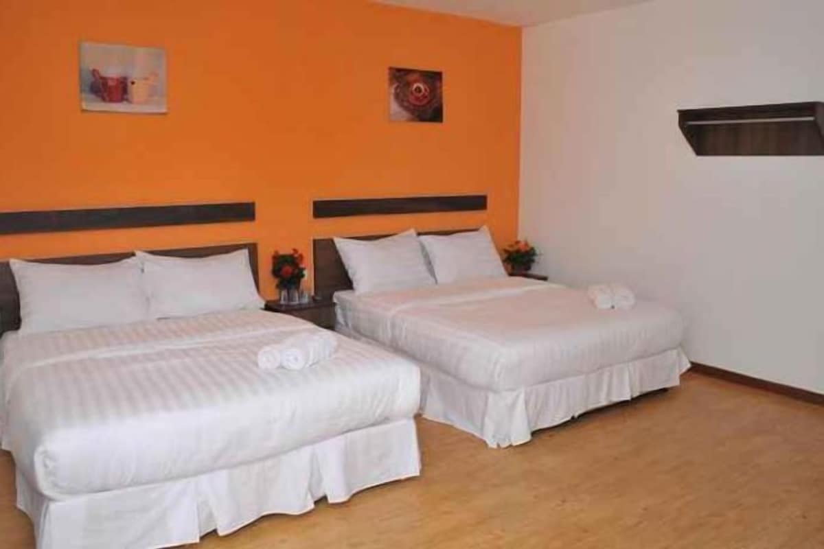 Une chambre d’hôtel avec deux lits, un plancher en bois et un mur de couleur orange unie.