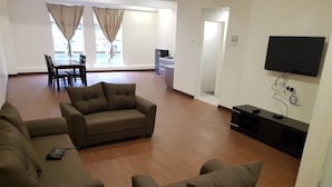 Un salón amplio con un conjunto de sofás, un televisor de pantalla plana montado en la pared y un comedor con sillas y una mesa.