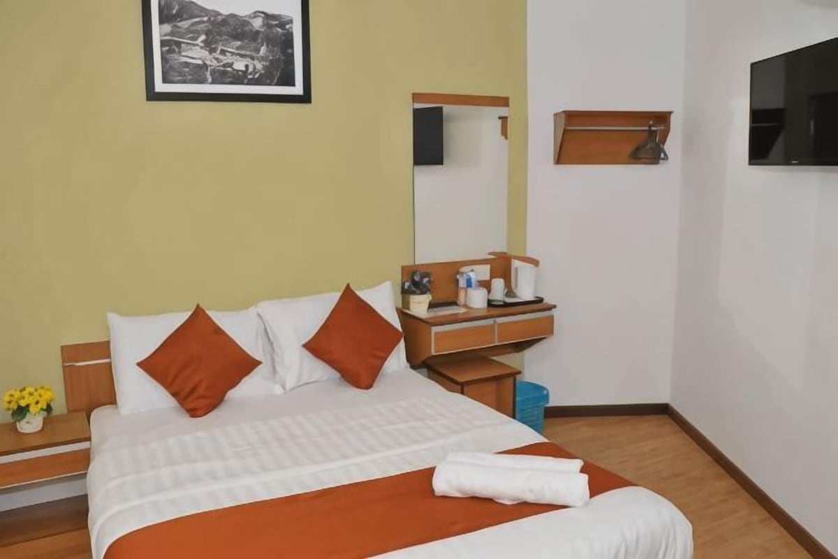 Une chambre d’hôtel avec un lit, une table de chevet, un miroir, une télévision et un tableau encadré au mur.