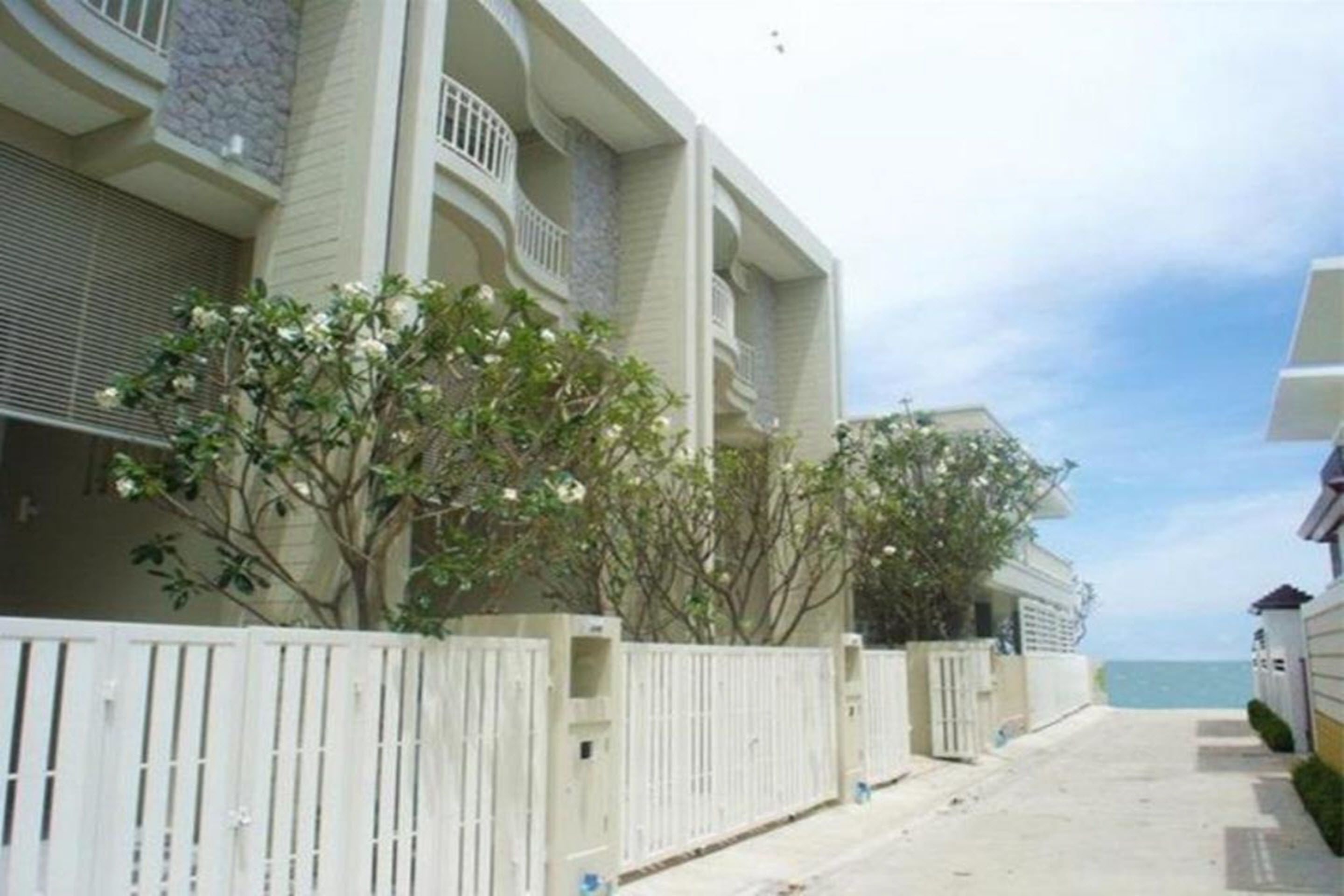 A two-story building with balconies, a gated entrance, and a view of the sea.
