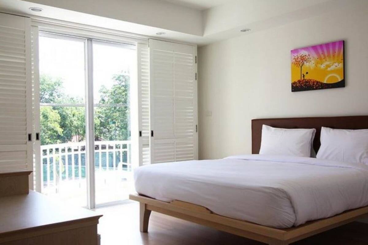 Un dormitorio con cama, un cuadro y un balcón con contraventanas blancas.