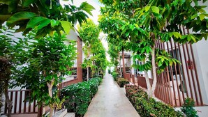 A narrow pathway flanked by lush greenery and wooden railings, leading to a building with white walls and a balcony. - Baanloksouylokchay (Hua Hin)