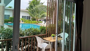 A balcony with a view of a swimming pool, surrounded by greenery and palm trees. - Baanloksouylokchay (Hua Hin)