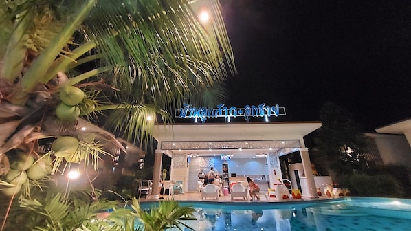 A hotel with a pool area, palm trees, and a sign with Thai script.