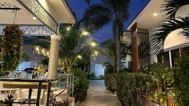 A well-lit outdoor area with a pool, lounge chairs, and palm trees. - Baanloksouylokchay (Hua Hin)