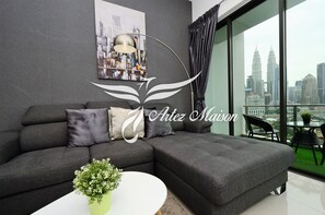A modern living room with a grey sofa, a white coffee table with a plant, a cityscape view through large windows, and a framed cityscape artwork on the wall.