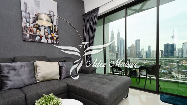 Ein modernes Wohnzimmer mit einem grauen Ecksofa, einem weißen Couchtisch und Blick auf eine Stadtlandschaft durch große Fenster.