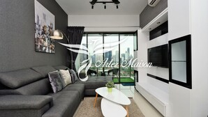 Ein modernes Wohnzimmer mit einem grauen Sofa, einem weißen Couchtisch und einem großen Fernseher an der Wand.