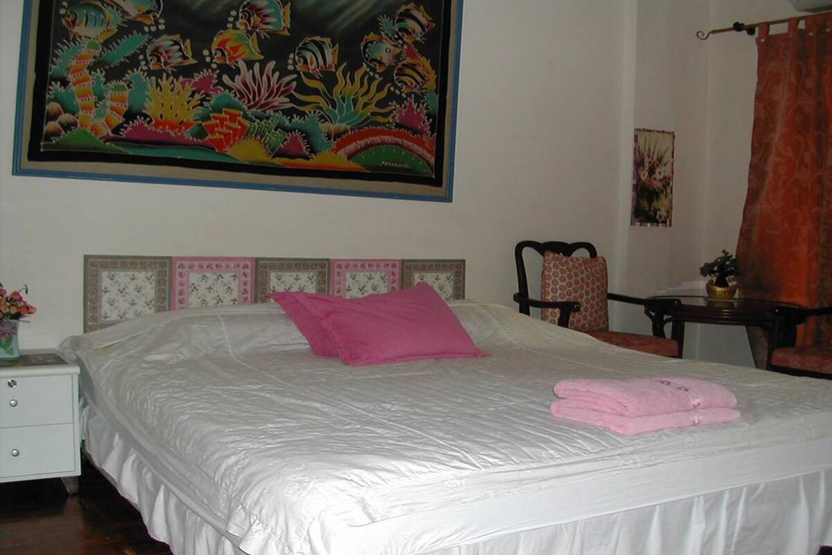 Un dormitorio con una cama grande, un almohón rosa y un cuadro sobre la cama.