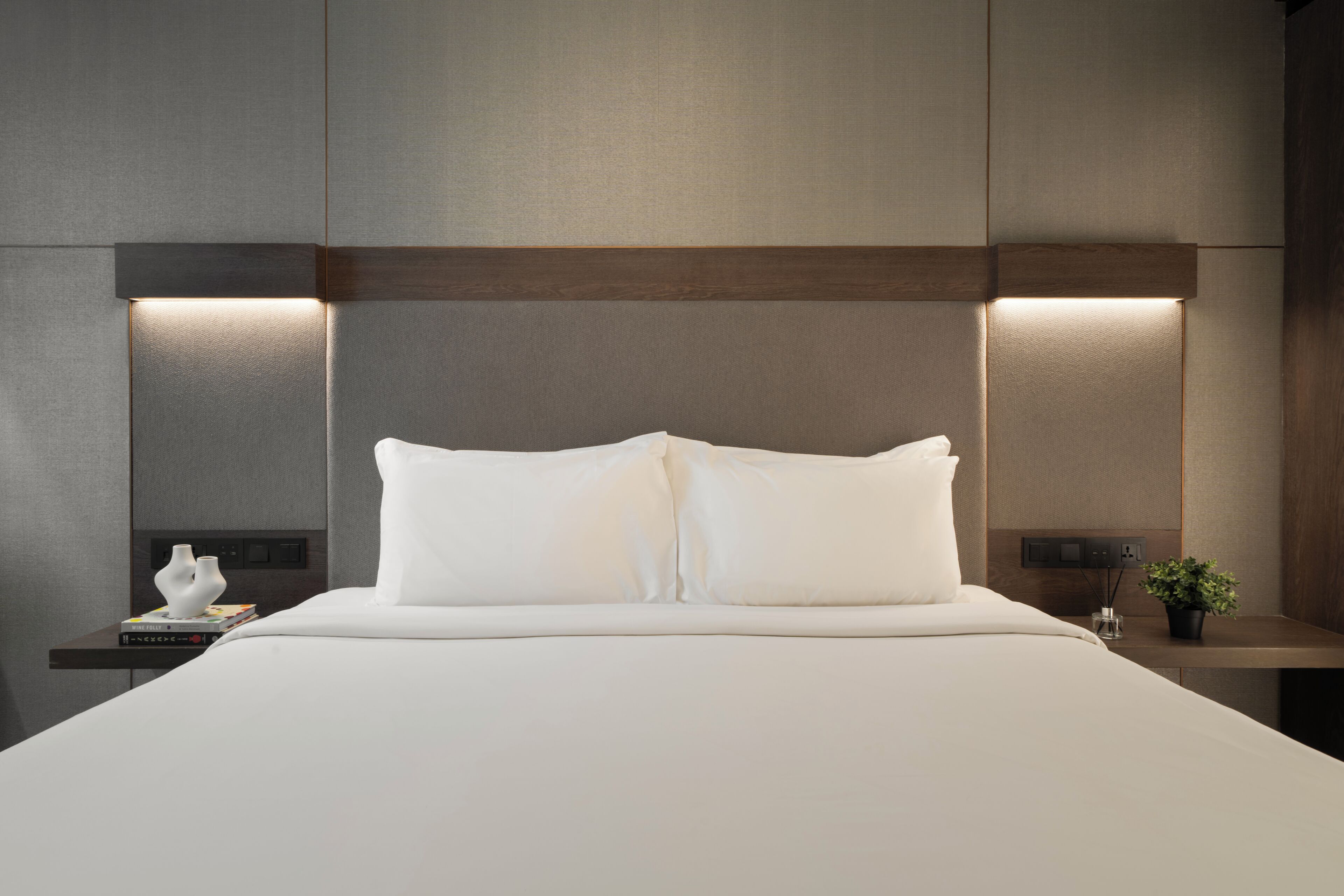 A modern hotel room with a large bed, bedside tables, and wall-mounted lighting.