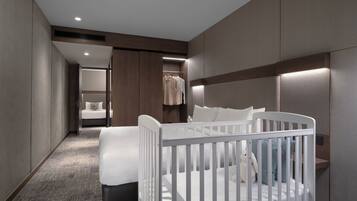 A modern hotel room with a crib, a bed, a walk-in closet, and a bathroom.