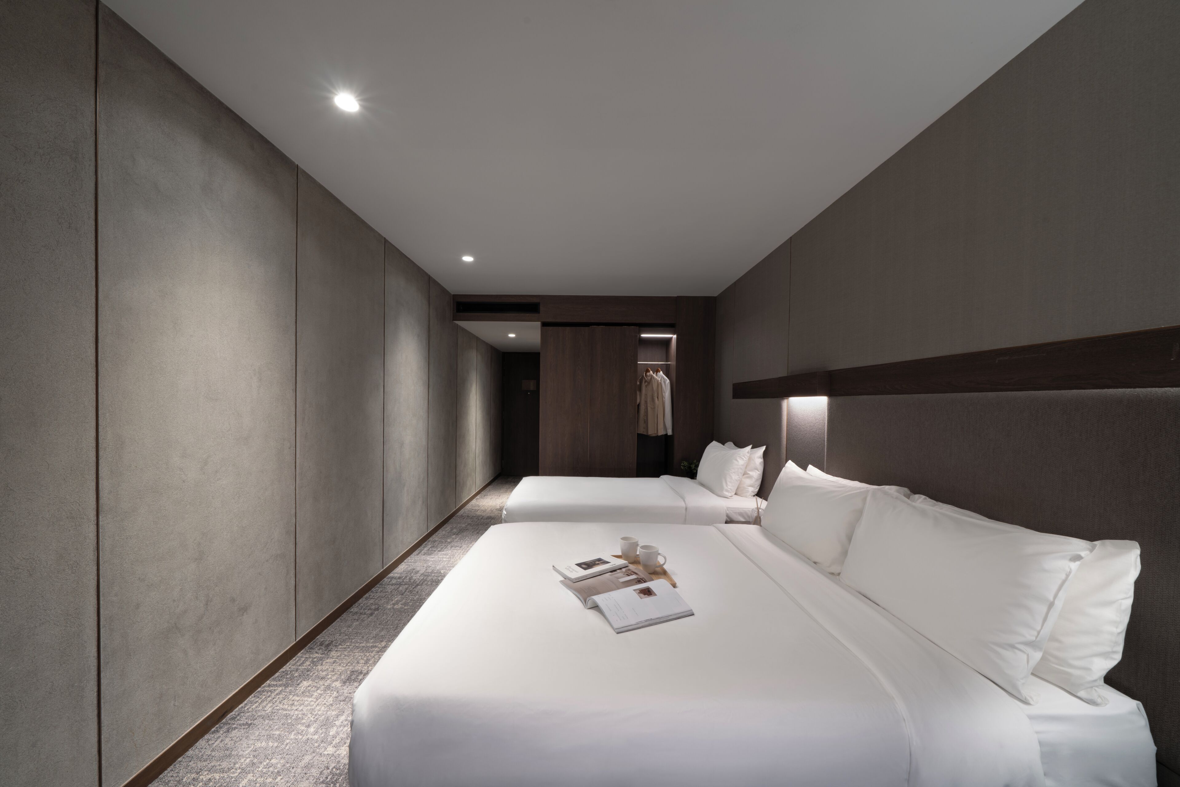 A modern hotel room with two beds, a walk-in closet, and a hallway.
