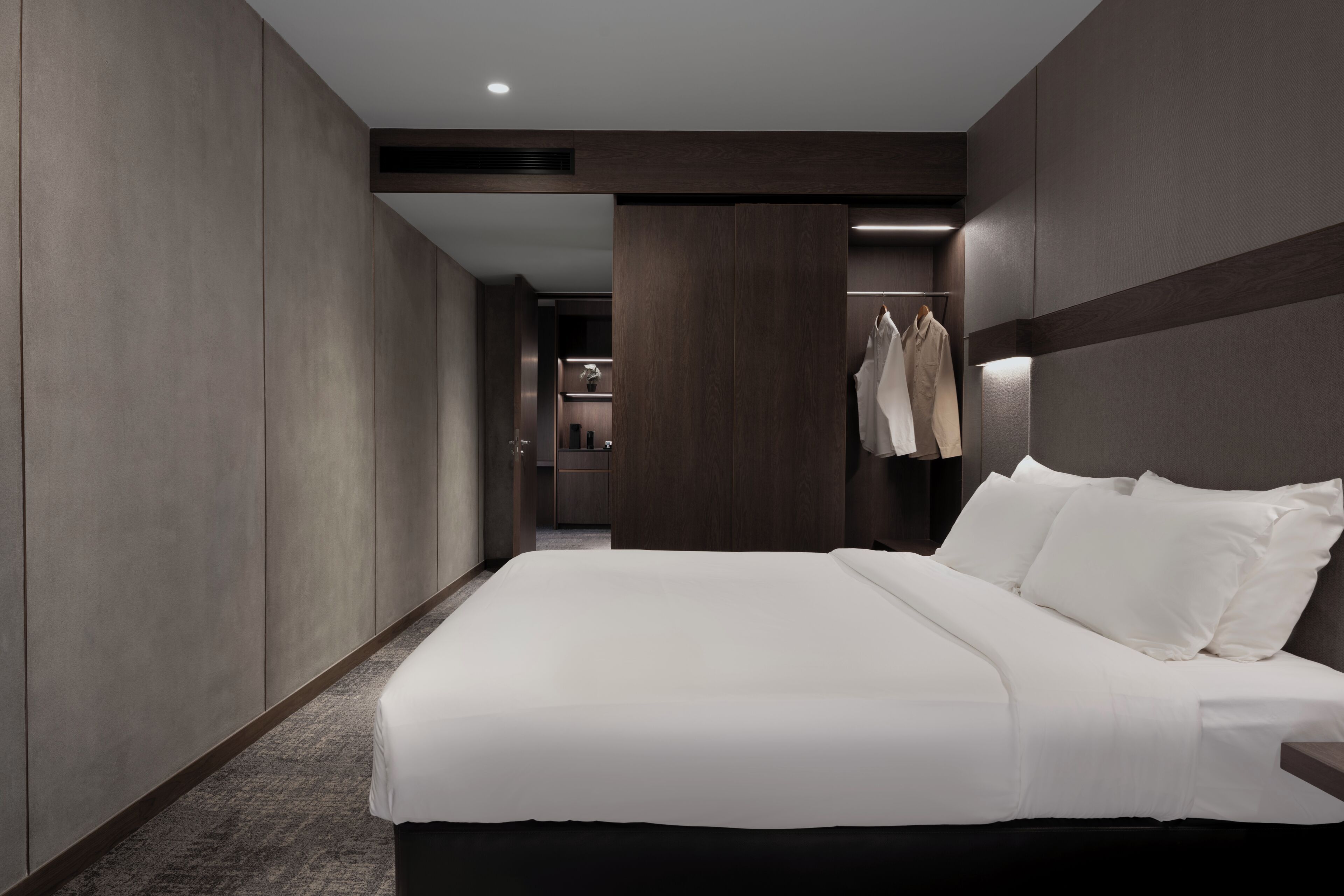 A modern hotel room with a large bed, a wardrobe, a mirror, and a clothing rack.