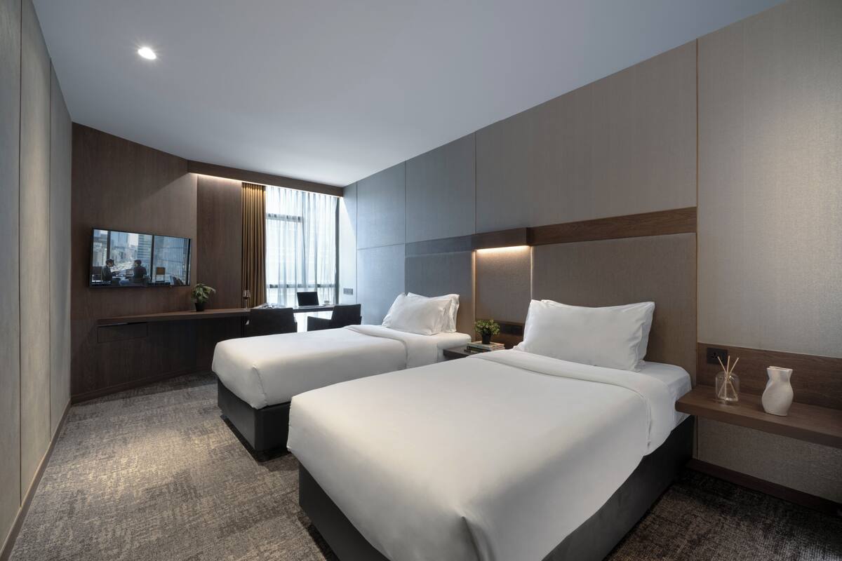 A hotel room with two beds, a desk, a TV, and a large window.