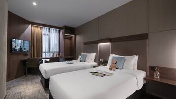 A hotel room with two beds, a desk, a TV, and a large window with curtains.