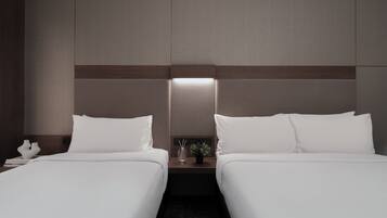 A hotel room with two single beds, a nightstand with a lamp, and a small table with a plant.