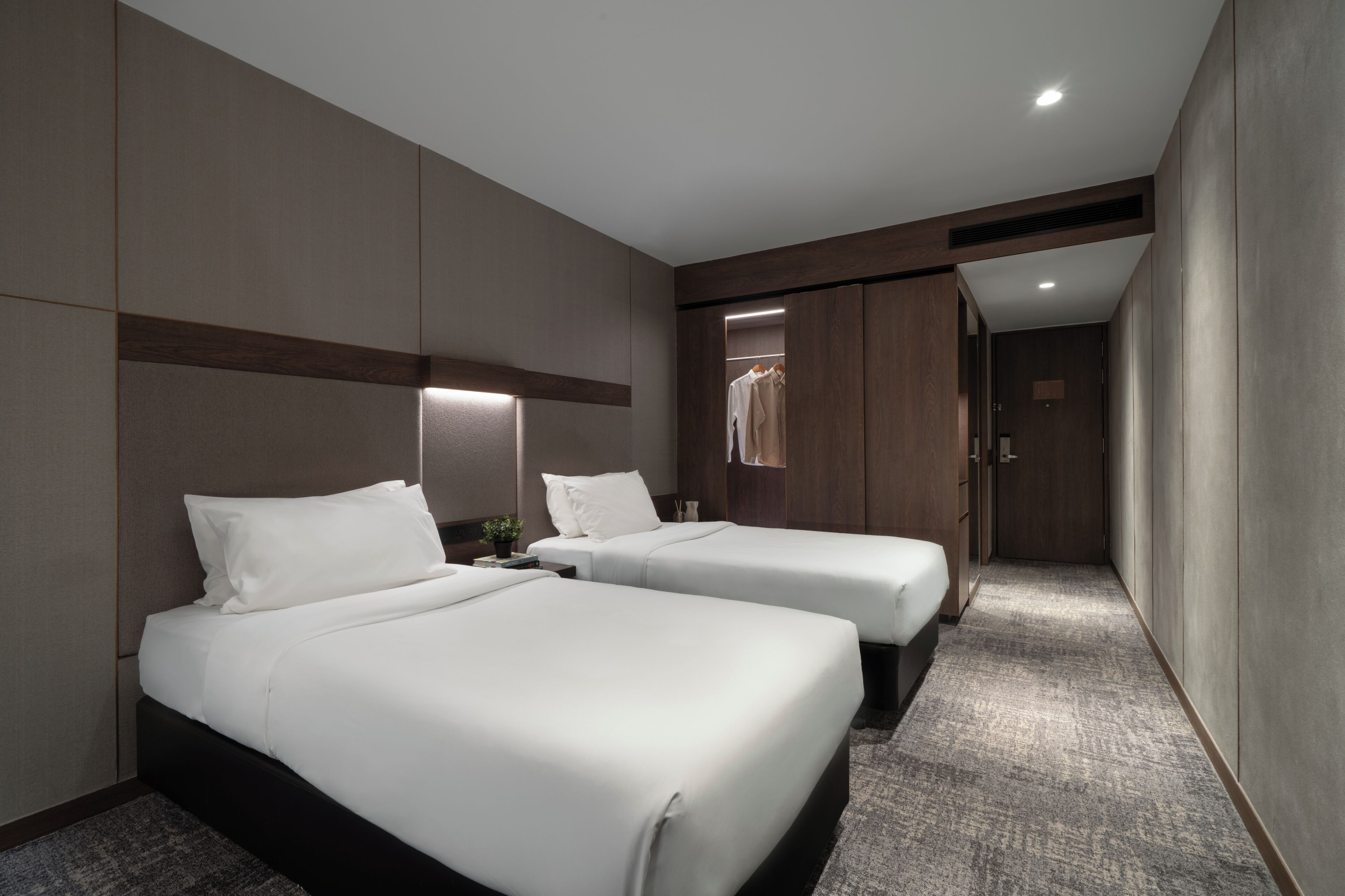 Een hotelkamer met twee bedden, een kledingkast en een gang.