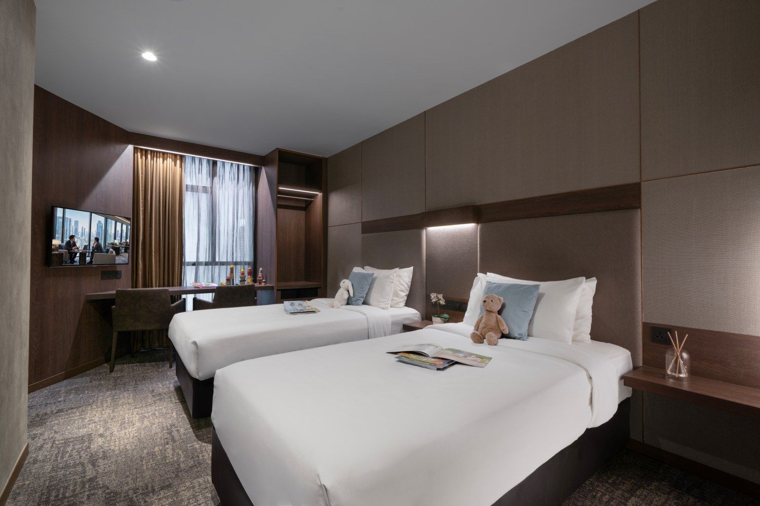 A hotel room with two beds, a desk, a chair, a television, and a window with curtains.