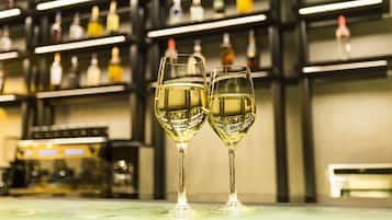 Two glasses of white wine on a bar counter with shelves of bottles in the background.