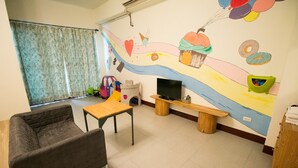 A cozy room with a sofa, a small wooden table, a TV, and a colorful mural on the wall. - Happy Hi B&B (Taitung)