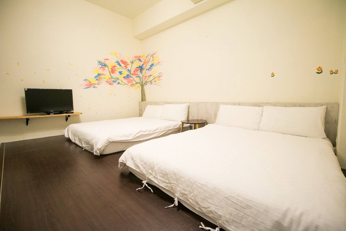 A hotel room with two single beds, a TV on a shelf, and a colorful wall mural.