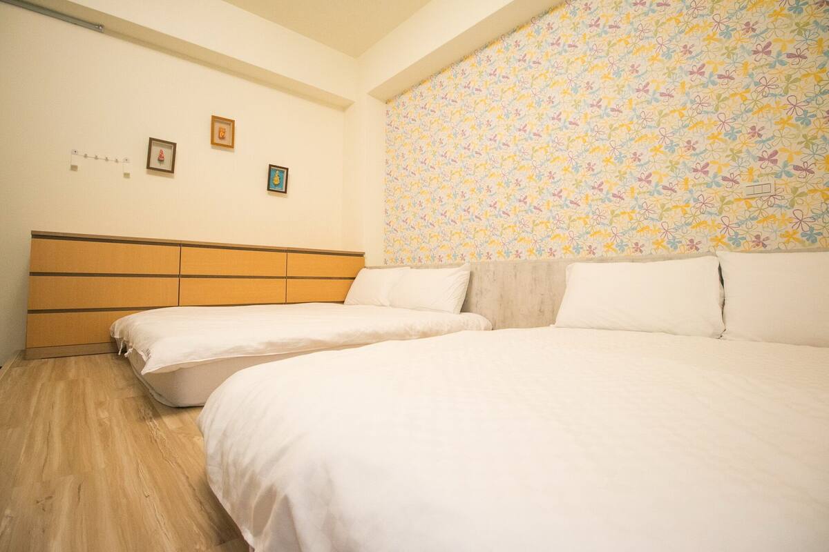 A bedroom with two beds, a wooden headboard, and a floral-patterned wall.