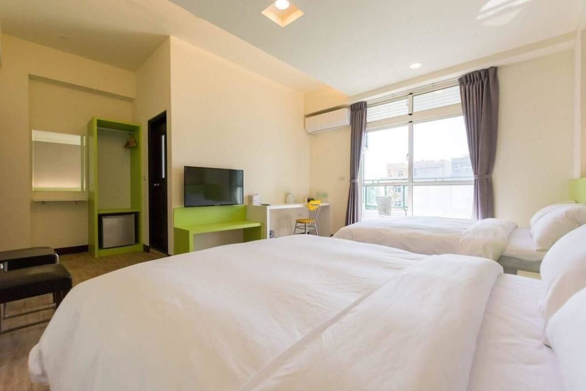 Una habitación de hotel con dos camas, televisión, escritorio y ventana con cortinas.