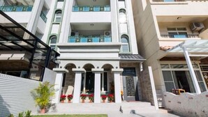 A multi-story building with a central entrance flanked by columns, a covered patio area, and a small garden with potted plants. - Pandora Elevator B&B (Taitung)