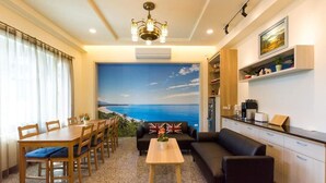 A hotel room with a dining area, a sofa, a kitchen, and a large window with a view of the sea. - Pandora Elevator B&B (Taitung)