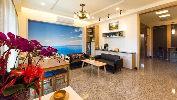 A modern living room with a sofa, coffee table, and a dining table. There is a kitchen area with a countertop and cabinets. - Pandora Elevator B&B (Taitung)