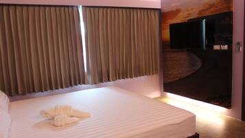 A hotel room with a bed, curtains, a television, and a wall mural.