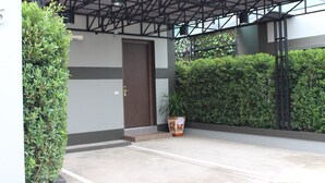 Una entrada de edificio con puerta, escalones, una planta en maceta y una reja de metal.