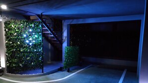 Un estacionamiento poco iluminado con un muro verde cubierto de follaje, una escalera y un suelo de hormigón.