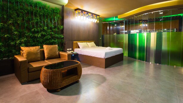 Un dormitorio moderno con cama, sofá, una mesa de centro de mimbre y una pared cubierta de plantas verticales.