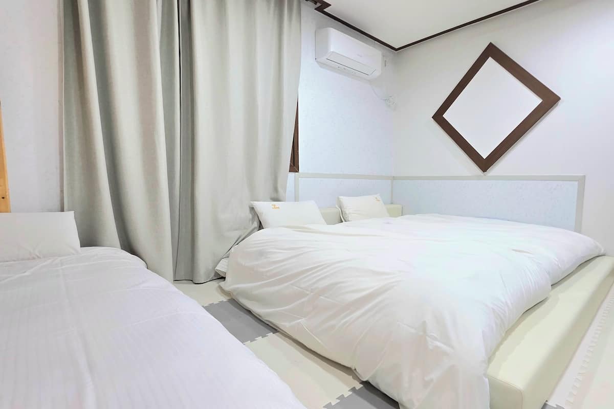 Habitación de hotel con dos camas, un ventanal con cortinas, un equipo de aire acondicionado y un espejo fijado a la pared.