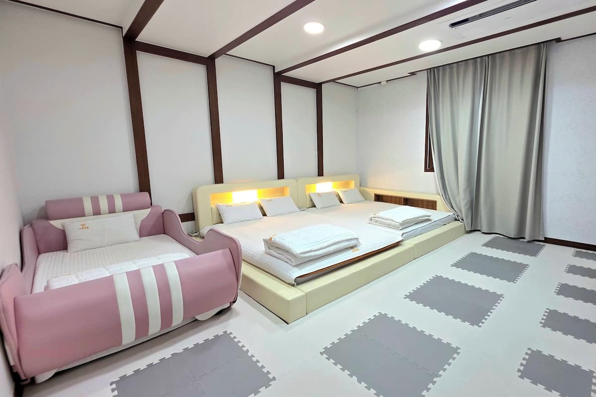 Un dormitorio con cama, sofá, escritorio y computadora, y una ventana con cortinas.