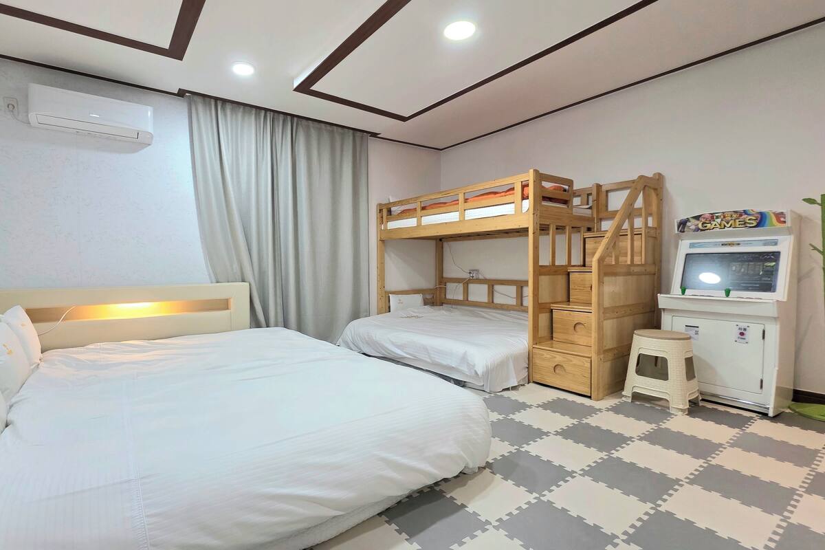 Habitación de hotel con dos camas, una litera, un mueble pequeño con televisor y un equipo de aire acondicionado.