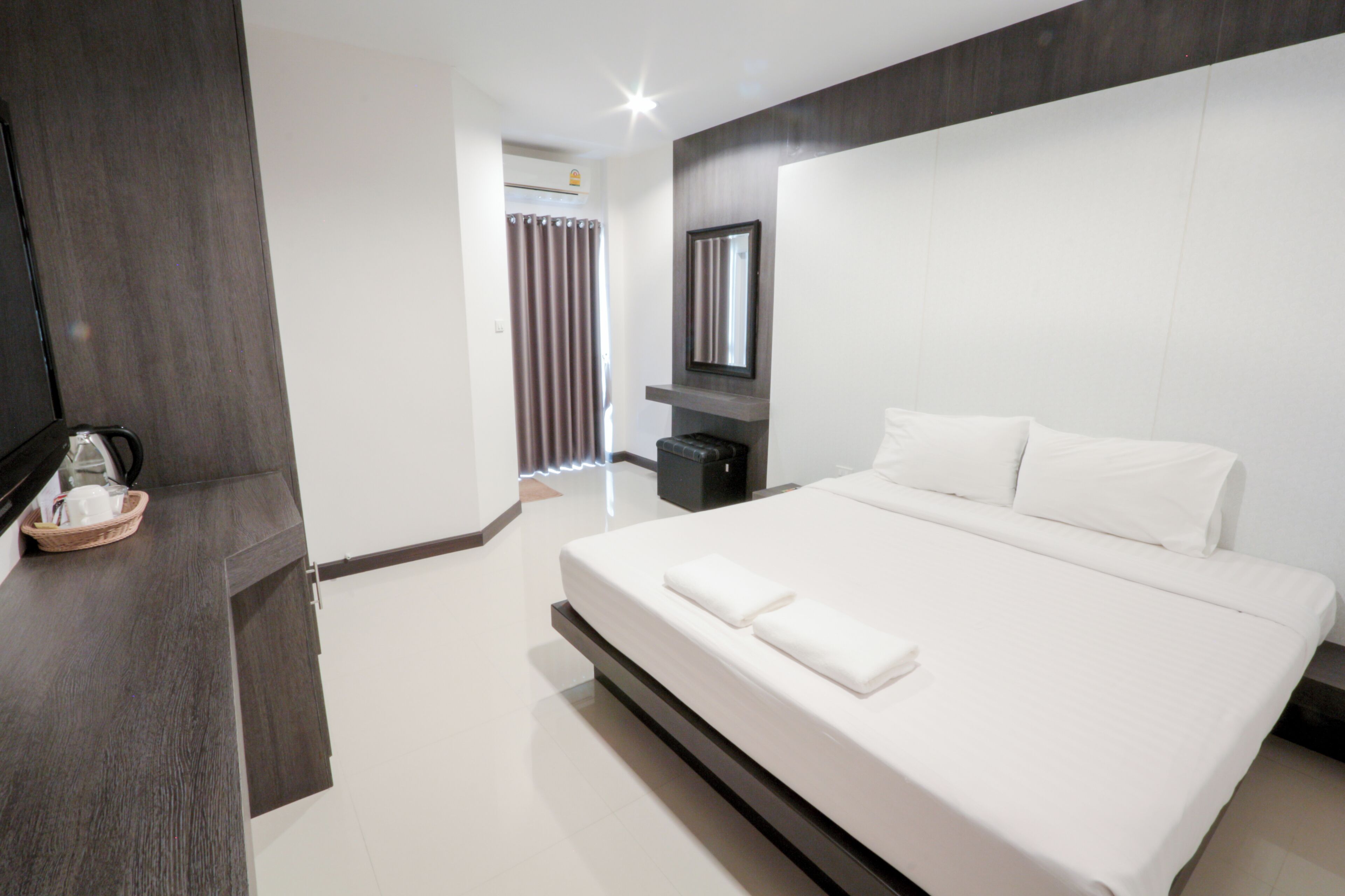 A modern hotel room with a large bed, a flat-screen TV, a bedside table, and a bathroom with a shower curtain.
