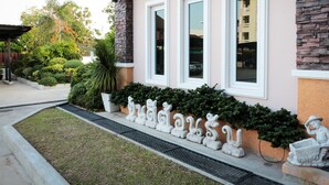 Un edificio con fachada de piedra, amplias ventanas y un jardín bien cuidado con estatuas decorativas.