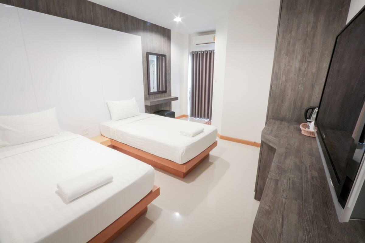 Habitación de hotel con dos camas, televisión, espejo y ventana con cortinas.